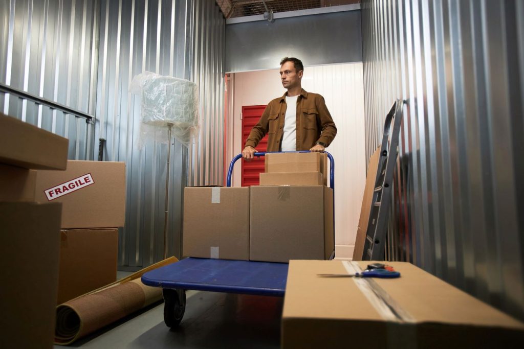 A man pushes a handcart filled with cardboard boxes into a storage unit.